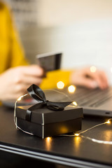 Black gift box - shopping online through a laptop with a credit card. A girl makes a purchase from home via the Internet. Cyber monday and black friday concept
