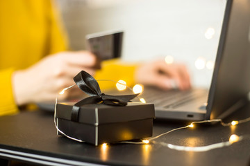 Black gift box - shopping online through a laptop with a credit card. A girl makes a purchase from home via the Internet. Cyber monday and black friday concept