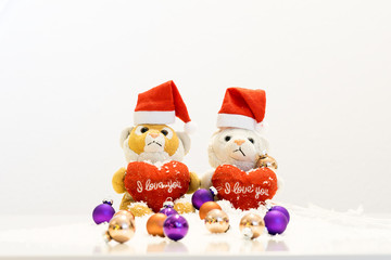 Zwei Teddybören mit Weihnachtsmützen sitzen auf Schnee mit Christbaumkugeln im Vordergrund