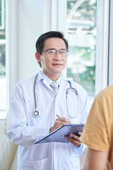 Mature asian general practitioner talking to patient and taking notes