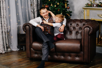 Obraz premium Father and son in New Year costumes are sitting on the couch near the Christmas tree