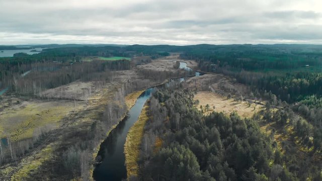 Aerial, rising, tilt, drone shot, of a river, surrounded by leafless, autumn forest. There¬¥s some sunlight, on a cold, cloudy, fall day, in Juuka, North Karelia, Finland