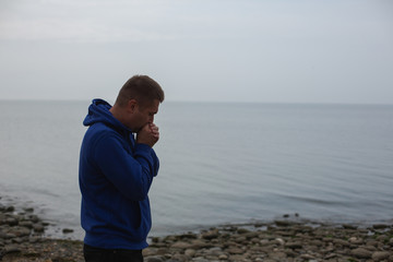Lonely Young Man in a Hoodie Standing on the Sea Background. Gloomy Weather.