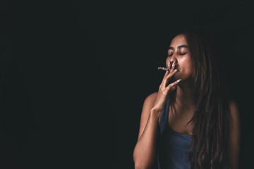 Obraz premium Woman Smoking a Cigarette on Black Background. Portrait of a beautiful girl, letting out smoke cigarettes. Women addicted smoking. People having problem and smoking cigarette.