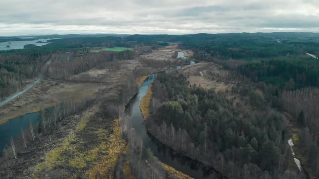 Aerial, drone shot, flying over a river surrounded by leafless autumn forest, on a cloudy fall day, in Juuka, Pohjois-Karjala, Finland