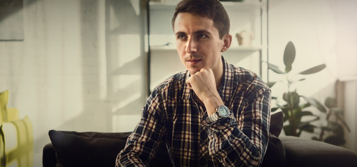 Portrait of a guy in the studio. Bright interior. Plaid shirt. Cinematic grading.