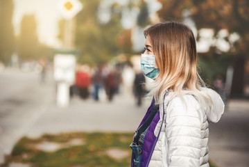 the girl is standing by the road in a protective medical mask. Dense smog in the streets of the...