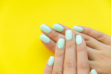 Tender hands with perfect blue manicure on trendy pastel yellow background. Place for tex