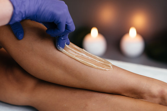 Midsection of beautician waxing woman's leg at salon