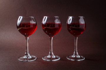 3 small glasses of red liquor on elegant dark brown background