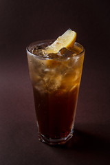 Glass of ice tea with ice and slice of lemon on elegant dark brown background