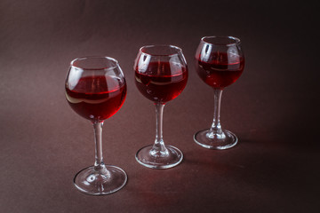 3 small glasses of red liquor on elegant dark brown background