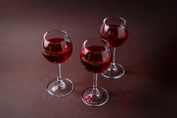 3 small glasses of red liquor on elegant dark brown background