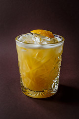 Glass of yellow alcohol cocktail with ice and slice of lemon on elegant dark brown background