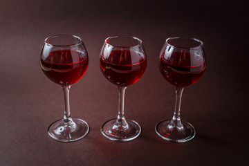 3 small glasses of red liquor on elegant dark brown background