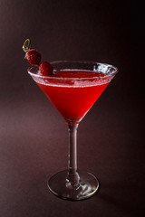 Glass of red cocktail with paspberries on elegant dark brown background