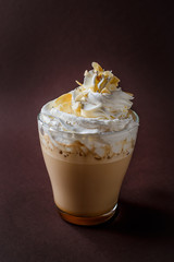 Glass of coffee with whipped cream and almonds shaving on elegant dark brown background