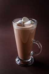 Glass of cacao with three marshmallows on elegant dark brown background