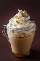 Glass of coffee with whipped cream and almonds shaving on elegant dark brown background