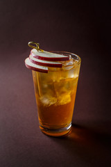 Glass of whisky cocktail with slices of apple on elegant dark brown background