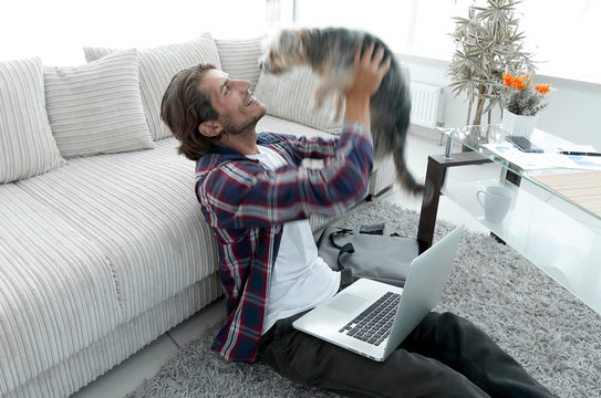 stylish guy playing with his dog, sitting by a spacious living room.