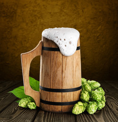 Wooden mug with beer and hops on a dark background.