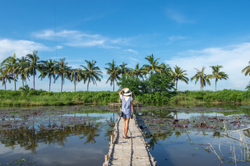 The woman on the bamboo bridge in the lotus pond  background and coconut trees.