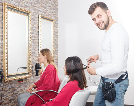 Young man professional hairdresser cut female's hair in salon