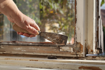 Worker removing oil window glazing putty using putty knife tool, old window restoration