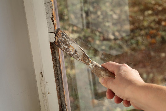 Worker removing oil window glazing putty using putty knife tool, old window restoration