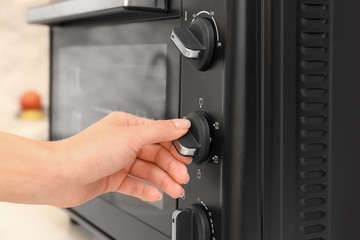 Woman adjusting electric oven in kitchen