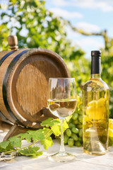 Barrel, glass and bottle of white wine on table in vineyard