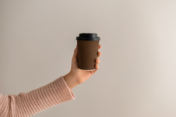 Woman holding paper coffee cup on light background