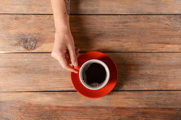 Female hand with cup of aromatic coffee on wooden background, top view
