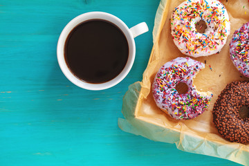 Delicious glazed donuts in box and cup of coffee on turquoise blue surface