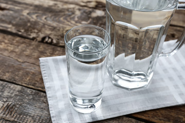 Glass and jug with fresh water on wooden table