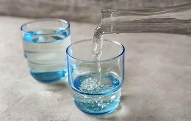 Pouring of fresh water from bottle into glass on table