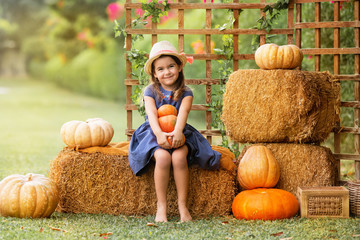 Cute little girl sitting on the haystack with pumpkins in the garden