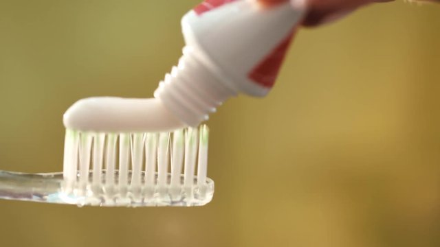 Close up squeezing white toothpaste on toothbrush. Macro shot of toothpaste coming out of tube. Everyday teeth care. Morning teeth hygiene