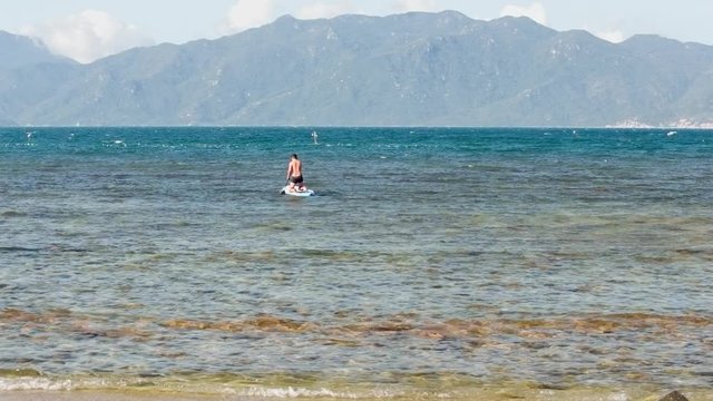 man figure standing on knees rows paddleboard in ocean