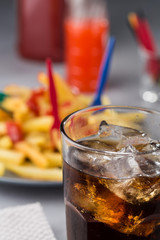 fizzy drink with ice in a glass on the background of a plate with fried potatoes