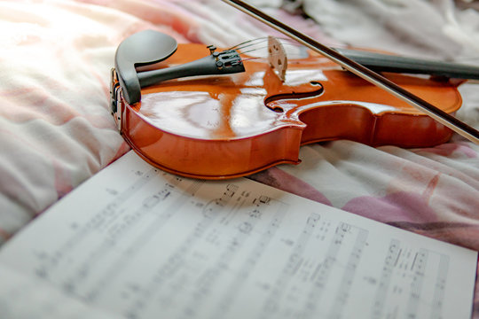 Vintage violin and the sheet of music note on the flowery bed in girly bedroom. Playing music instrument at home concept