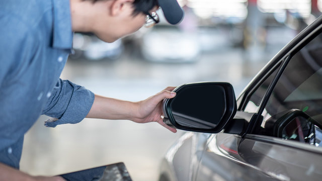 Young Asian auto mechanic holding digital tablet checking car wing mirror. Mechanical maintenance engineer working in automotive industry. Automobile servicing and repair concept