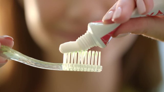 Morning teeth brushing in bathroom. Close up woman hands squeezing toothpaste on toothbrush. Personal oral hygiene and teeth care. White toothpaste coming out of tube