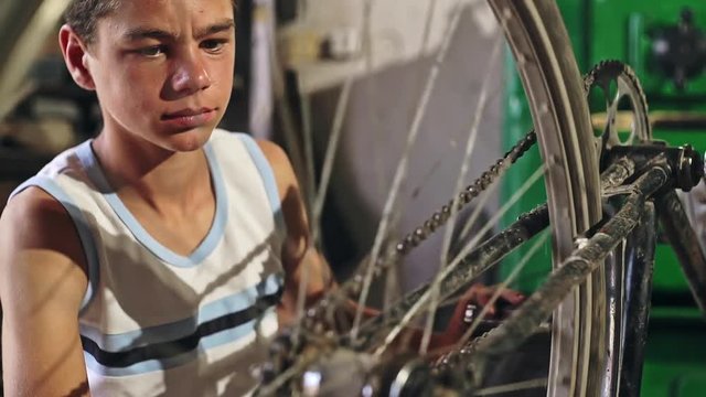 Crop teen boy touching pedal of broken bicycle while trying to fix it in workshop.