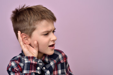 Young boy holding his hand on the ear and trying to hear what someone is saying 