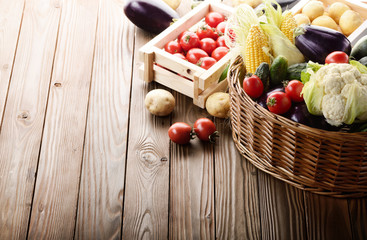 Basket of Organic Vegetable Food Ingredients and crates of potatoes and tomatoes on wood background