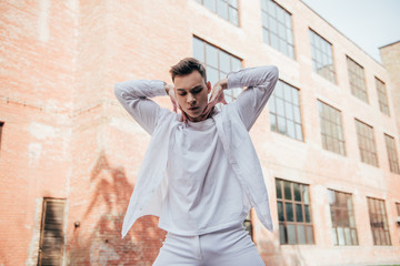 Obraz premium low angle view of handsome young man in white clothes dancing on urban street