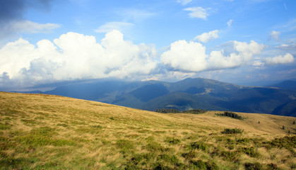 Fototapeta na wymiar big white clouds in the mountains on the peak, yellow grass, scenery view