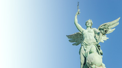 Top roof statue of sensual renaissance era angel with wings in front of blue sky in Vienna,...